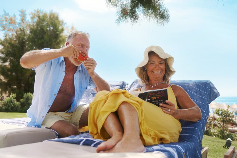 Par skrattar och njuter av att läsa en bok i en solstol