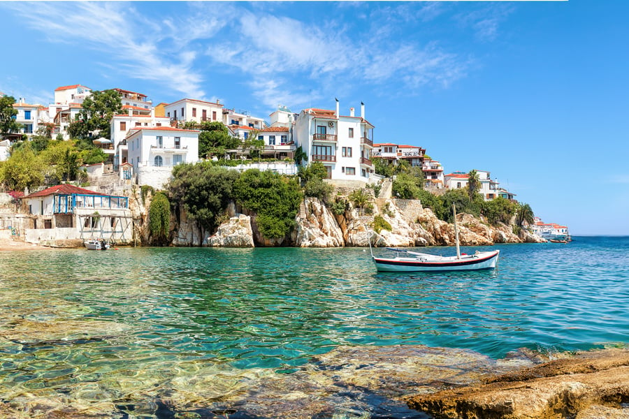 Vy över en kustremsa i Grekland, havet glimmrar i grönt, en båt ligger och guppar i bukten
